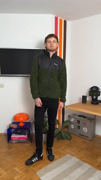 Giacca di fleece verde con parte anteriore in nylon nero, chiusura con zip e maniche lunghe. Indossata con pantaloni neri e scarpe nere con strisce bianche.