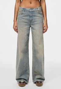 Jean en denim à jambes larges dans un lavage bleu clair. Dispose d'une taille haute, d'un design traditionnel à cinq poches et d'une décoloration subtile le long des jambes.