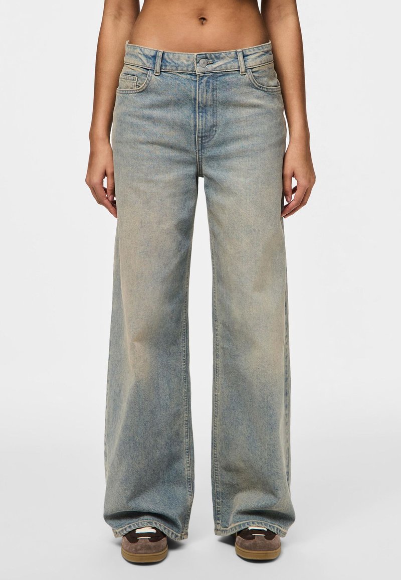 Jean en denim à jambes larges dans un lavage bleu clair. Dispose d'une taille haute, d'un design traditionnel à cinq poches et d'une décoloration subtile le long des jambes.