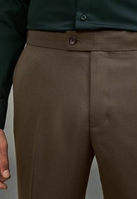 Brązowe spodnie o fakturze z gładkim paskiem w talii i pojedynczym zapięciem na guzik, stylizowane w dopasowanym kroju z delikatnym wzorem w romby.