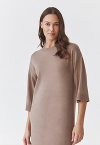 Robe tricotée marron clair avec un col rond et des manches trois-quarts. Texture douce avec des accents côtelés aux poignets et à l'ourlet.