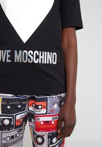 Person wearing a black shirt with "LOVE MOSCHINO" text and pants with colorful retro cassette tape prints, standing against a plain background.