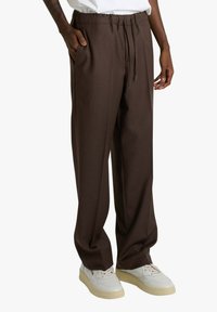 Pantaloni marroni su misura con vita elastica e dettaglio coulisse; realizzati in tessuto liscio. Presentano tasche laterali e vestibilità comoda.