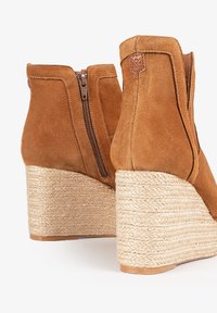 Bottine en daim marron à semelle compensée avec un talon en jute texturé, dotée d'une fermeture éclair sur le côté et d'un accent logo simple près du haut.