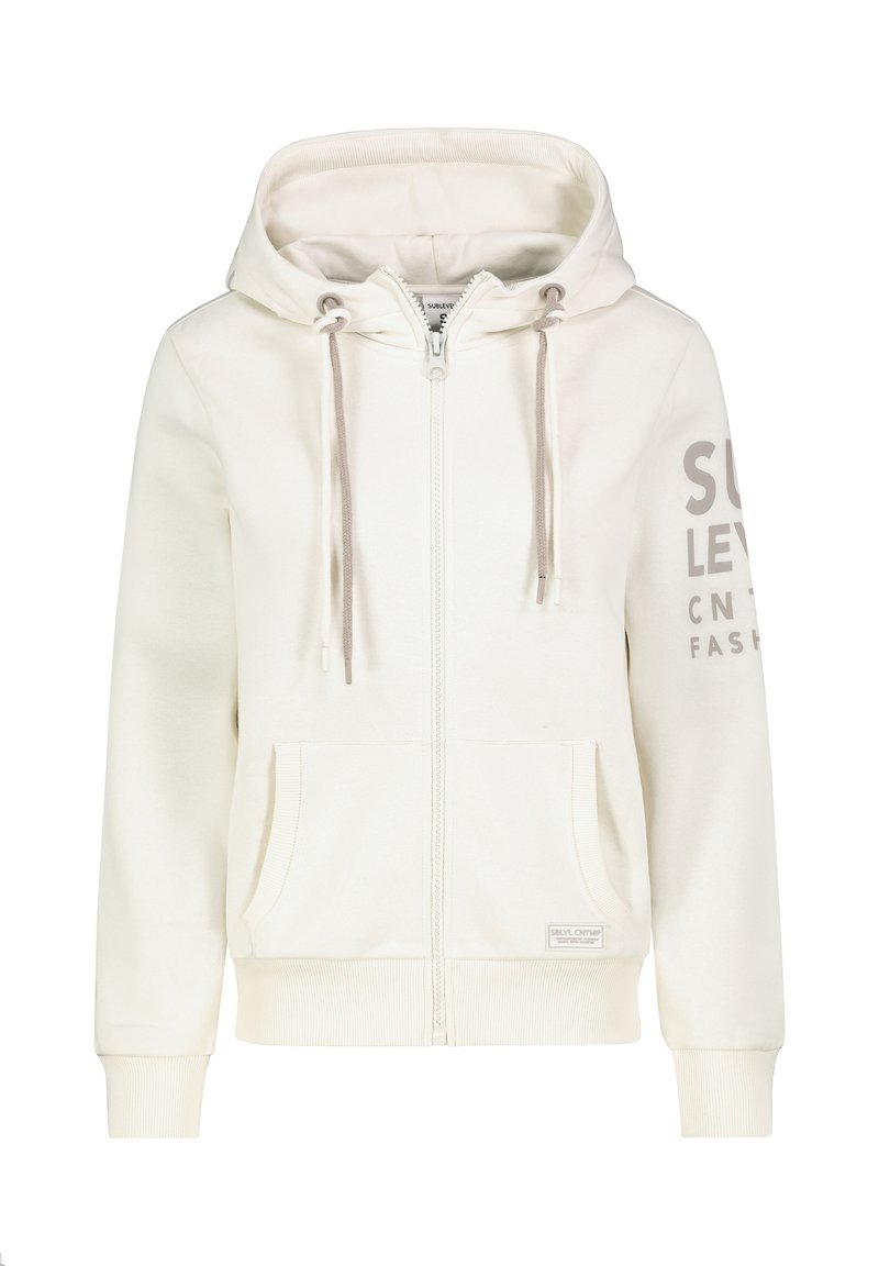 Helle beige Zip-Hoodie mit geräumiger Kapuze, beigen Kordeln, Vordertaschen und dem Aufdruck "SULY LEVEL" in Grau auf dem linken Ärmel.