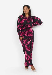 Conjunto negro con un patrón floral abstracto en rosa. Incluye una camisa abotonada con mangas abullonadas y pantalones sueltos. Tejido suave, con cinturilla elástica.
