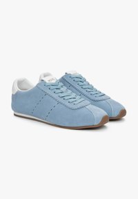 Jasnoniebieskie zamszowe sneakersy z białymi akcentami, cechujące się eleganckim wzornictwem, okrągłym noskiem, szczegółowym szyciem i brązową gumową podeszwą.