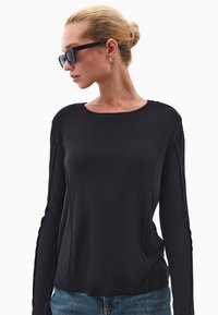 Czarny długi rękaw top z miękkiego materiału z okrągłym dekoltem, z subtelnymi szwami bocznymi, w połączeniu z niebieskimi dżinsami.