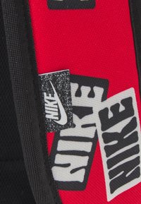 Tela roja y negra con múltiples logotipos de Nike en negro y blanco en parches cosidos.