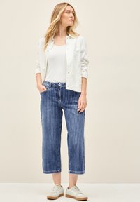 Pantalones de mezclilla azules cortos con rayas blancas verticales, combinados con una camiseta sin mangas blanca y una chaqueta ligera, complementados con zapatillas blancas.