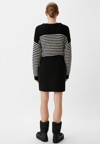 Gestreifter, schwarzer und weißer Strickpullover mit einem verkürzten Design, kombiniert mit einem schwarzen Rock. Schwarze, plüschige Knöchelstiefel runden den Look ab.