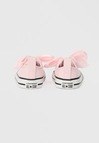 Růžové plátěné tenisky s velkými saténovými stuhami na zadní straně, černobílým logem a gumovými podrážkami, které předvádějí klasický nízký design.