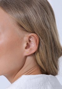 Gold stud earrings with two spherical accents, worn on the ear, featuring a simple design and smooth surface texture.
