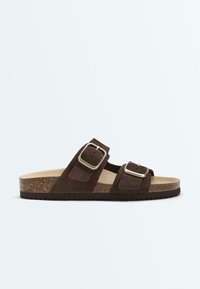 Sandale mule en daim marron avec deux boucles argentées réglables, semelle intérieure en liège et semelle noire rainurée, vue de profil sur fond blanc.