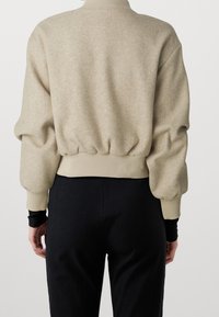 Beżowy sweter z mieszanki wełny, z okrągłym dekoltem, bufkami oraz marszczonym dołem. Połączony z czarnymi spodniami w prążek.