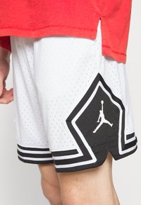 Weiße, durchlöcherte Basketballshorts mit schwarzen Akzenten und einem auffälligen Jumpman-Logo. Sie verfügen über ein geometrisches Design und einen gestreiften Saum.