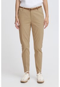 Pantalon chino kaki à coupe fuselée, doté d'une ceinture marron, de poches avant, porté avec des baskets blanches. Le matériau semble léger et lisse.