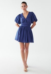 Kurzes blaues Kleid mit Puffärmeln, V-Ausschnitt, gerafftem Oberteil und elastischem Bund. Abgeschlossen mit gewelltem Saum und aus leichtem Stoff gefertigt.