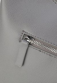 Borsa a tracolla in pelle grigia con texture, dotata di una tasca con zip, caratterizzata da una zip in argento lucido e dettagli di cucitura lungo il lato.