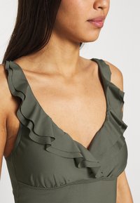 Fato de banho verde-azeitona com alças de ombro em renda e design em formato de V, feito de material suave com detalhes franzidos no busto.