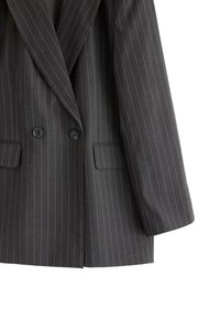 Dobbeltbrystet blazer i mørkegrå med hvide striber, to forlommer og sorte knapper; struktureret revers og glat tekstur.