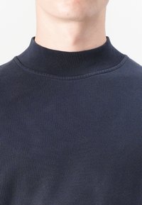 Sötétkék, magas nyakú pulóver sima anyagból. Zökkenőmentes gallérral és testhezálló fazonnal rendelkezik. Nincsenek látható minták vagy díszítések.