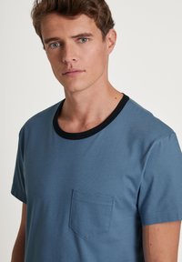 Blauw T-shirt met korte mouwen en een ronde zwarte kraag, voorzien van een klein borstzakje en een zachte textuur.