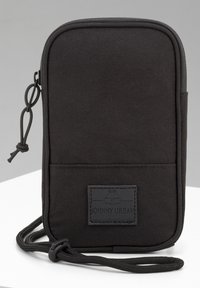 Malá černá látková crossbody taštička se zipovým uzávěrem, nastavitelným šňůrkovým popruhem a decentní obdélníkovou etiketou na přední straně.