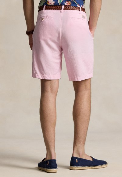 Ροζ σορτς από ύφασμα με λεία υφή, με δύο πίσω τσέπες και τελείωμα που καταλήγει πάνω από το γόνατο, φορεμένα με ναυτικούς εσπαντρίγιες.