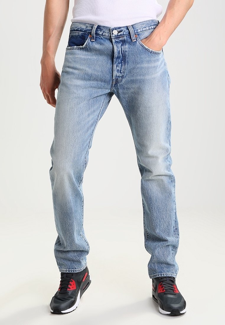 Faded blue denim jeans with a straight cut, five pockets, and visible stitching details, paired with black and red athletic sneakers.