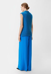 Ärmelloses Stricktop in leuchtendem Blau mit strukturierter Oberfläche und hohem Kragen, kombiniert mit blauen, weit geschnittenen Hosen.