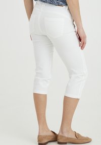 Pantaloni bianchi a cappotto con una vestibilità aderente, orli arrotolati e tasche posteriori. Tessuto leggero con una leggera elasticità e texture liscia.
