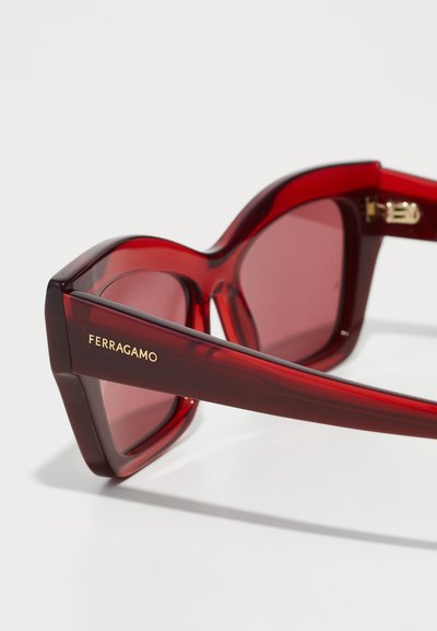 Gafas de sol rojas de gran tamaño con un acabado brillante, que presentan lentes degradados y la marca "FERRAGAMO" en dorado en el lateral.