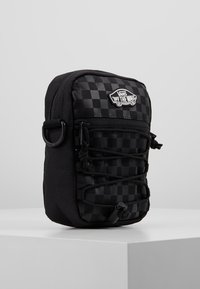 Schwarze Schachbrett-Tasche mit strukturiertem Design, ausgestattet mit elastischen Schnurdetaillierungen, einem oberen Reißverschluss und einem Vans-Logo-Patch auf der Vorderseite.