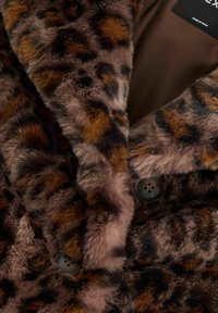 Manteau en fausse fourrure à imprimé léopard, avec une texture douce, des motifs bruns et noirs, et des boutons foncés. Doublure intérieure d'une couleur marron unie.