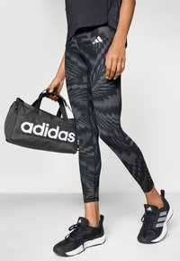 Sorte leggings med mønster og geometrisk design, parret med en sort Adidas træningstaske med markante hvide logoer, samt sorte træningssko.