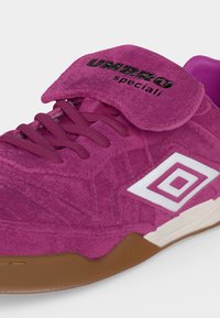 Παντόφλα Umbro Speciali από μοβ σουέντ με διπλωμένη γλώσσα, κλείσιμο με κορδόνια, λευκό λογότυπο διπλού διαμαντιού και σόλα από καουτσούκ.