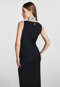 Czarna sukienka bez rękawów o dopasowanym kroju z detalem w postaci guzików z tyłu. W zestawie z wzorzystą apaszką w kolorze białym i czarnym.