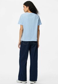 Camiseta de manga corta azul con lunares negros, de corte relajado. Combinada con vaqueros de pierna ancha de denim oscuro y zapatillas blancas. Diseño simple y casual.