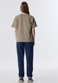 Beige katoenen t-shirt met korte mouwen, relaxte pasvorm, gecombineerd met losse blauwe denim broek. Zichtbare stiksels en taps toelopende manchetten. Grijze sneakers.