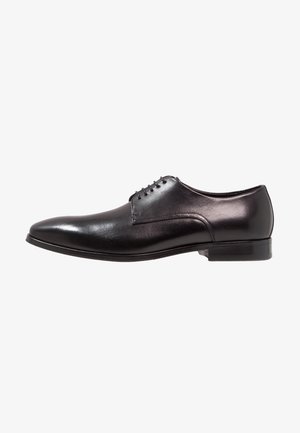 Chaussure habillée en cuir noir avec une finition lisse, bout arrondi et cinq œillets pour les lacets. Talon légèrement surélevé et détails de couture minimaux.