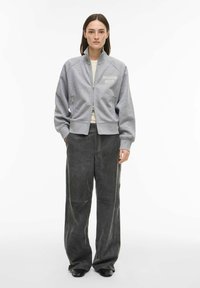 Grauer Sweatshirt mit Reißverschluss und dem Schriftzug "ROUGE EDIT", mit hohem Kragen und Raglanärmeln, kombiniert mit lockeren dunkelgrauen Hosen und schwarzen Schuhen.