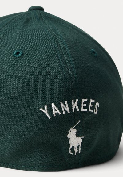 Tumši zaļš beisbola cepure ar baltu izšūtu "YANKEES" tekstu un mazu balto polo spēlētāja logo uz sāna. Tekstūrēta auduma, izliekts vizieris.
