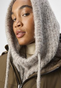 Brown zip-up jacket with a thick, textured beige scarf. The scarf has a soft, knitted appearance and drapes around the neck.