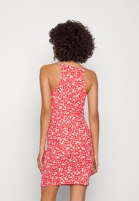 Punainen kukkakuosisekoituspuku, jossa on vartalonmyötäinen muotoilu, hihaton malli ja kaareva takahelma. Materiaali näyttää sileältä ja siinä on hieman joustavuutta.