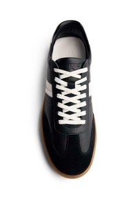 Zapatilla de cuero negra con rayas blancas, presenta una punta redondeada, superficie texturizada y cordones blancos. Suela de goma de color contraste goma.