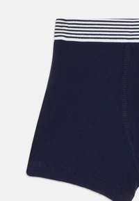Boxer aderenti blu navy con un elastico in vita a strisce bianche e nere e cuciture visibili lungo i lati e le aperture delle gambe.