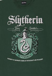 Zielona koszulka bawełniana z napisem "Slytherin", symbolem węża i ozdobną grafiką tarczy. Drukowany wzór w białym i jasnym zielonym kolorze.