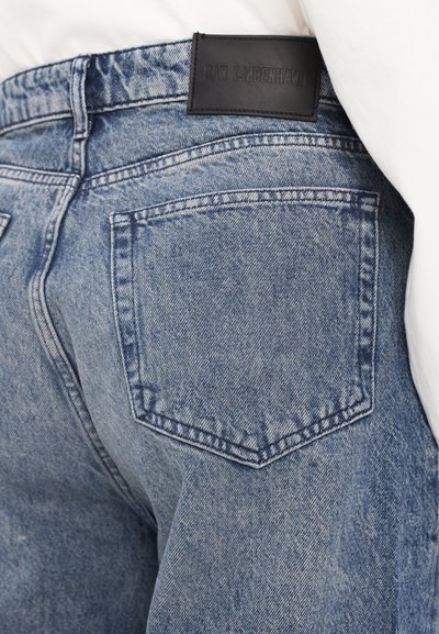 Hellblaue Denim-Jeans mit einem klassischen Fünf-Taschen-Design, sichtbaren Nähten und einem schwarzen Leder-Brand-Tag am hinteren Bund.