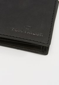 Black leather wallet with embossed "TOM TAILOR" logo. Features simple design, sleek shape, and visible stitching details.